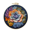 A circular embroidery hoop containing a colorful embroidered succulent floral design on a dark navy fabric background, shown against a plain white studio background.