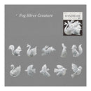 A gray square card showing the name 'Fog Silver Creature' at the top left, a small inset photo labeled 'HANDMADE' at top right, and multiple small silver animal and bird figurines arranged across the lower half. The product appears to be a collection of silver creature/craft pieces shown in a catalog-style layout.