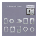 A set of silver foil embossed frames in various shapes including ovals, rectangles, hearts, and circles, displayed on a lavender background with a small product packaging insert in the upper right.