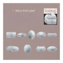 A sheet of silver foil labels with various decorative shapes and scalloped edges, displayed on a dusty mauve background with text reading 'Silver Foil Label' and a small 'HANDMADE' label sample in the top right.