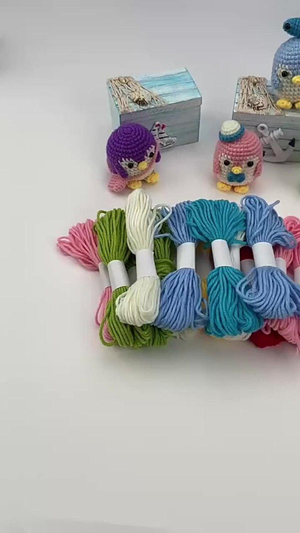 Colorful skeins of yarn tied together with small toy figures in the background on a light gray surface.