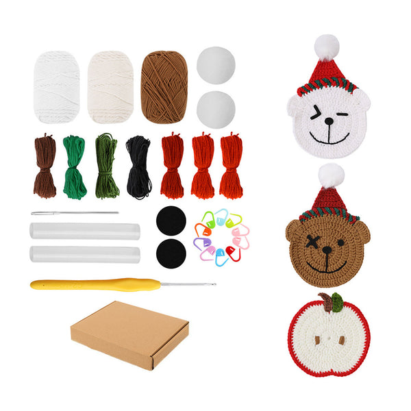 Crochet kit with yarn balls, thread bundles, a yellow crochet hook, stitch markers, two completed bear hats, an apple coaster, and a brown cardboard box on a white background.