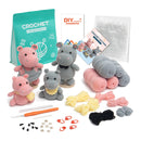 Crochet hippo toy kit with three crocheted hippo toys, a teal bag of yarn, rolled pink and gray yarn, yellow and black yarn, crochet hooks, stitch markers, clips, and pattern booklets on a white background.