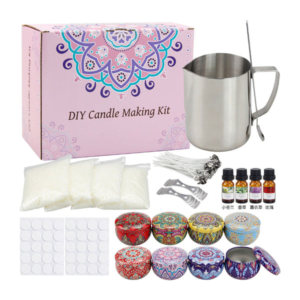 DIY candle making kit with a pink patterned box, stainless steel pouring pot and spoon, wax wick packs, fragrance oil bottles, wicks, metal tins, and decorative lids on a white background.