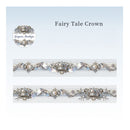 A decorative silver and white embroidered band labeled 'Fairy Tale Crown' with a circular logo reading 'Gaspard's Handicraft.' The design shows ornate mirrored embroidery with ribbon-like folds, floral motifs, and crown details on a pale blue-to-white gradient background.