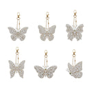 Six butterfly-shaped drop earrings in gold-tone metal pavé-set with clear stones, arranged in two rows of three on a plain white background.