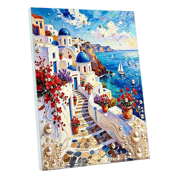 A 3D-effect diamond painting canvas featuring a vibrant Mediterranean coastal scene with white buildings, blue domes, red flowers, and sailboats on a blue sea under a cloudy sky.