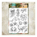 A sheet of clear stamp designs featuring black line drawings of ocean and beach-themed motifs, including jellyfish, seahorse, turtle, octopus, dolphin, starfish, crab, whale, and shells, displayed on a textured beige background with a tropical beach scene header.