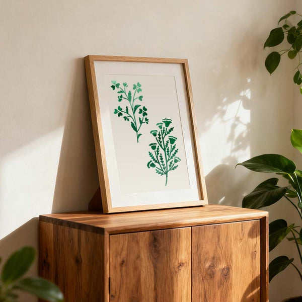 Framed artwork with green plant design on a wooden cabinet against a light wall.