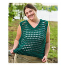 A woman outdoors wearing a sleeveless, open-knit crocheted top in dark green, paired with khaki pants. She is smiling and holding the hem of the top slightly to show its drape.