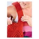 A close-up of a woman wearing a chunky, textured red crochet shoulder bag with a wide strap, holding the bag in place.