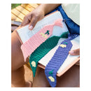 Three crocheted book bookmarks with tassels and small embroidered floral details are shown resting on an open book held by a person's hands and lap.