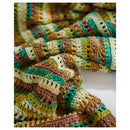 A close-up of a hand-crocheted striped blanket or throw in earthy tones of brown, green, beige, and mustard yellow, draped on a white surface.
