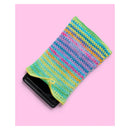 A colorful striped crocheted phone pouch holding a black smartphone, set against a solid pink background.