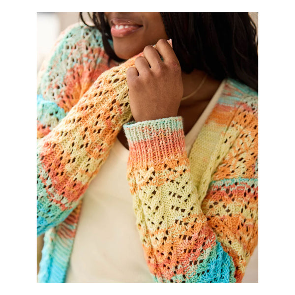 A close-up of a person wearing a colorful, open-front knit cardigan with a textured crochet pattern. The cardigan features pastel stripes of orange, yellow, pink, and turquoise blue.