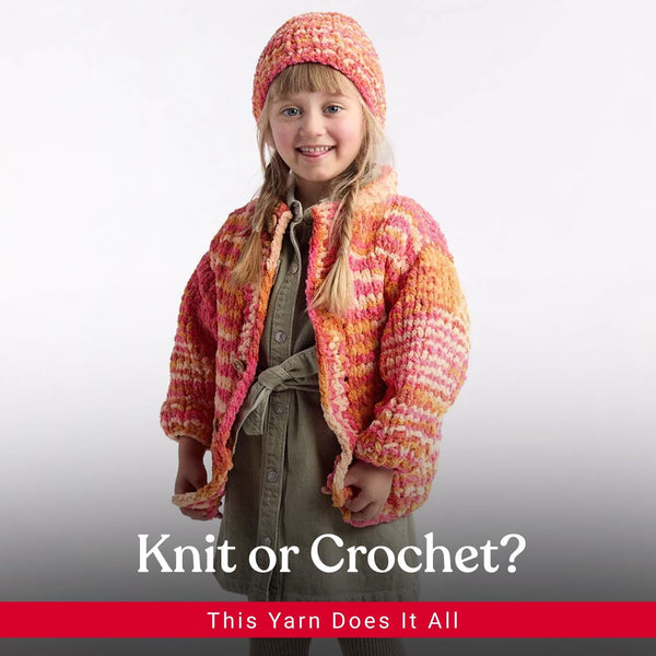 A young girl wearing a chunky hand-knit orange and pink beanie and matching cardigan over an olive green dress, posed against a light gray studio background with the text 'Knit or Crochet? This Yarn Does It All' at the bottom.