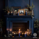 A dark blue fireplace mantel decorated with framed art, candles, and greenery, set against a matching dark blue wall.
