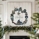 A distressed white wooden Christmas wreath wall sign with 'Merry Christmas' script, displayed above a decorated fireplace mantel with green garland and candles.