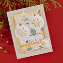 A handmade Christmas card with layered white and gold ornament designs, green holly accents, and the words 'magical moments,' photographed on a red background with holiday greenery and red ornaments around it.