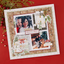 A square scrapbook layout or photo collage board styled with Christmas-themed paper cutouts, photos of a couple, decorative tags, pinecones, holly, and newspaper-style elements, placed on a red background with holiday greenery and red berries around it.