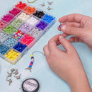 A close-up of hands threading a beaded cord with silver clasp ends, next to a clear plastic organizer filled with colorful round beads and a spool of seed bead cord on a light blue surface.