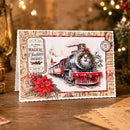 A handmade Christmas postcard featuring a vintage red steam locomotive train, a red poinsettia, and holiday-themed stamp designs, displayed on a wooden surface with a blurred festive background.