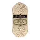 A skein of Scheepjes Stone Washed XL yarn in a warm cream-beige color, featuring its black and beige paper label in the center, set against a plain white background.