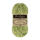 A skein of Scheepjes Stone Washed XL yarn in a light olive green color, featuring its original paper label.