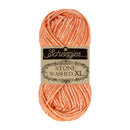 A skein of Scheepjes Stone Washed XL yarn in a peach-orange color, wrapped with its original paper label, on a solid white background.