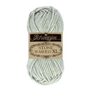 A skein of Scheepjes Stone Washed XL yarn in a pale sage green color, featuring its original paper label.