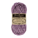A skein of Scheepjes Stone Washed XL yarn in a dusty lavender-purple color, featuring a beige paper label with black text, set against a plain white background.