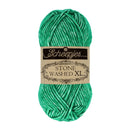 A skein of Scheepjes Stone Washed XL yarn in a vibrant emerald green color, featuring its original paper label wrapper, set against a plain white background.