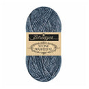 A skein of Scheepjes Stone Washed XL yarn in a heathered slate blue-gray color, featuring a beige paper label with black text, set against a plain white background.