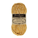 A skein of Scheepjes Stone Washed XL yarn in a warm golden yellow color, wrapped with a black and beige paper label, on a solid white background.