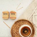 Two skeins of yarn with knitting needles on a textured surface, next to a woven basket and wooden bowl.