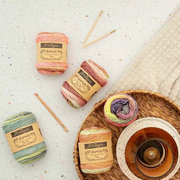 Colorful yarn balls with labels on a textured surface with knitting needles and a woven basket.