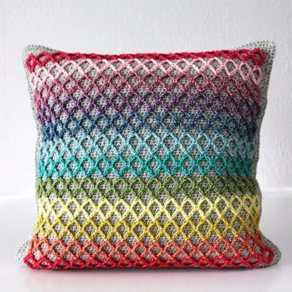 A square crocheted throw pillow with a colorful gradient pattern of red, orange, yellow, green, blue, and purple, set against a plain white background.
