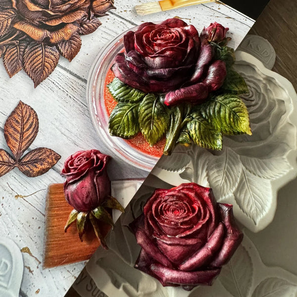 Three carved rose sculptures in shades of deep burgundy and purple, displayed alongside a white floral mold and a wooden carving block on a split white and gray wooden background.