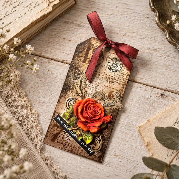 A decorative gift tag with a vintage map background, a red ribbon bow, and a 3D orange rose embellishment, styled on a rustic wooden surface with lace, dried flowers, and old paper.