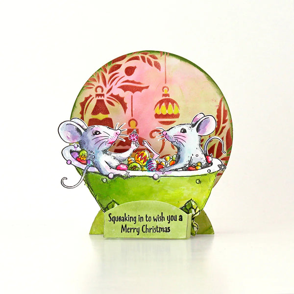 A handmade 3D pop-up Christmas card featuring two white mice in a green bathtub filled with colorful candies, set against a pink background with hanging ornaments. The card stands on a small green base with the text 'Squeaking in to wish you a Merry Christmas'.