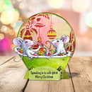 A festive Christmas card or decorative sign featuring two gray mice sitting in a green bathtub filled with colorful candies, with a pink and green holiday background and the text 'Squeaking in to wish you a Merry Christmas' on a small stand. The item is photographed on a wooden surface with blurred holiday lights in the background.