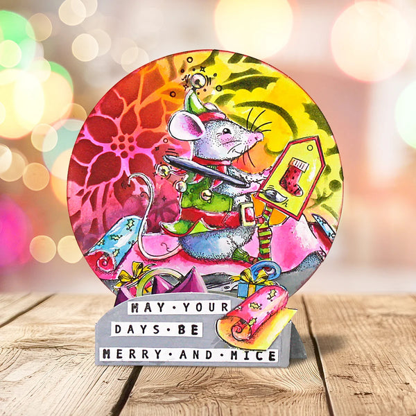 A colorful round decorative plaque featuring a cartoon mouse dressed as Santa, with a gray stand that reads 'HAY - YOUR DAYS BE MERRY AND MICE.' The plaque is photographed on a wooden surface against a softly blurred warm bokeh background.