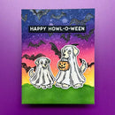 A square Halloween greeting card featuring two ghosted dogs, one holding a jack-o'-lantern, with the text 'HAPPY HOWL-O-WEEN' on a purple-to-yellow gradient background with bats and a green foreground, displayed against a purple backdrop.