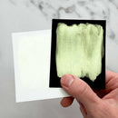Hand holding a small square of fabric with a greenish-yellow color swatch against a marble background