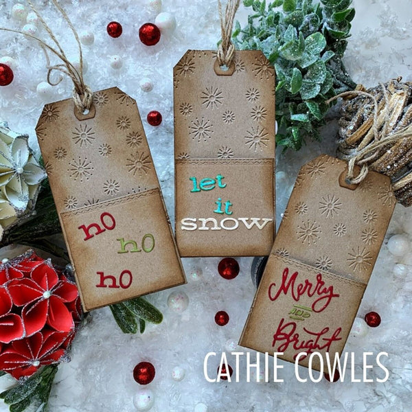 Three decorative kraft paper Christmas gift tags with stamped snowflake designs and holiday phrases 'no ho ho ho', 'let it snow', and 'Merry and Bright' arranged on a snowy white surface with red berries and greenery. The text 'CATHIE COWLES' appears at the bottom.