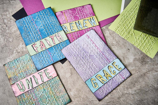 Decorative notebooks with embossed textures and motivational phrases on a textured surface.