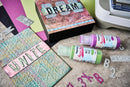 Crafting materials including stencils, spray paint, and letter stamps on a textured surface.