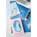 Two Christmas cards with cut-out designs and a die-cutting machine on a blue surface.