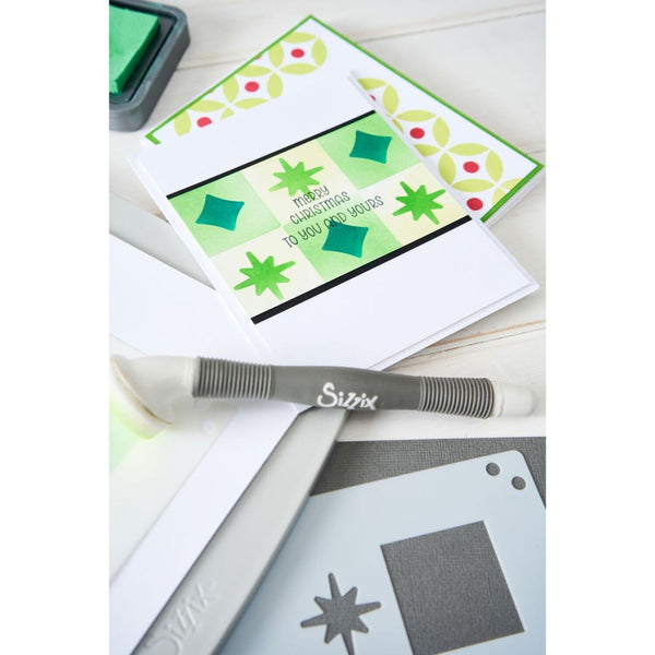 Card with green and red pattern, Sizzix tool, and stencils on a white background