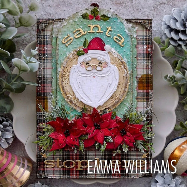 A handmade Christmas card or scrapbook art piece featuring a white Santa face cutout over a teal textured background, with red poinsettias, green foliage, plaid borders, and the words 'Santa' and 'stop'. The piece is photographed on a scalloped white dish surrounded by holiday greenery and pinecones.